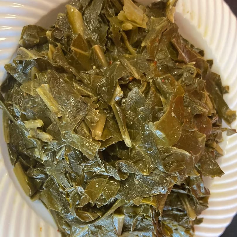 Close-up of a white plate filled with Aunt Berta's Kitchen's dark green, cooked collard greens.