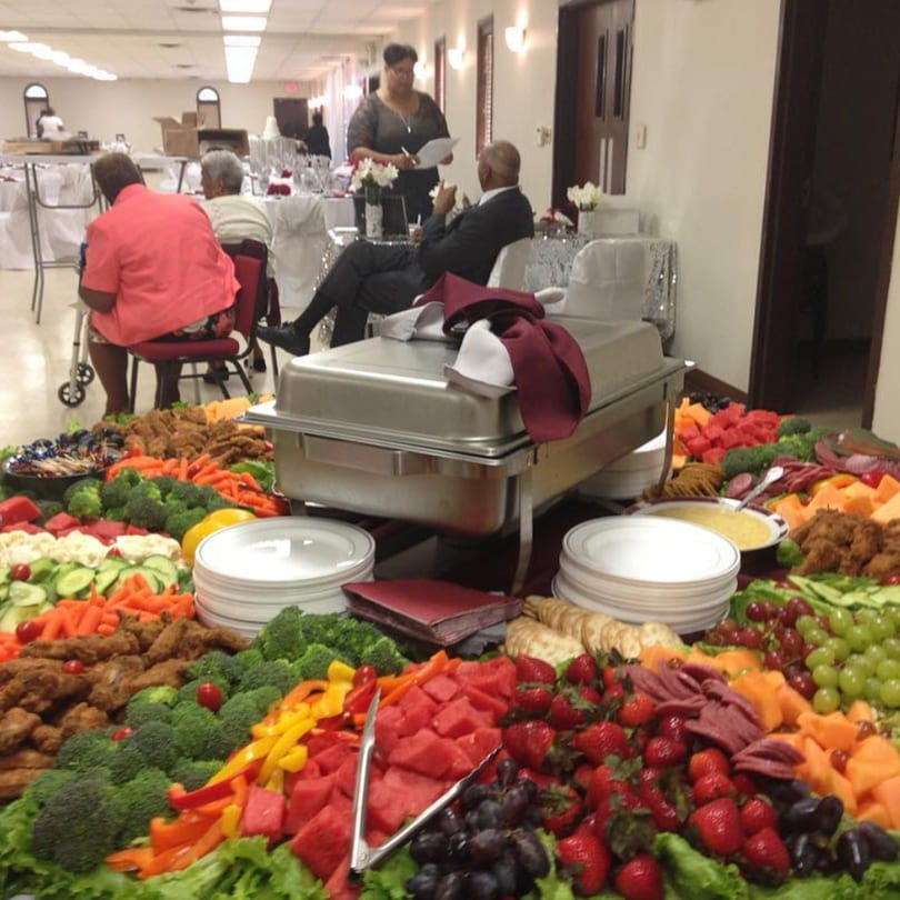 A large soul food buffet with fried chicken, vegetables, fruit, and a chafing dish.