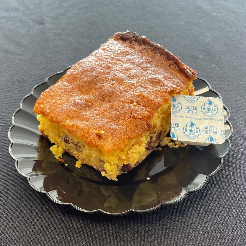 Aunt Berta's Kitchen cornbread with a side of butter on a black scalloped plate.
