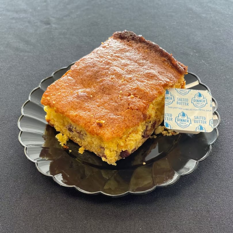 Aunt Berta's Kitchen's cornbread with a side of butter on a black scalloped plate.