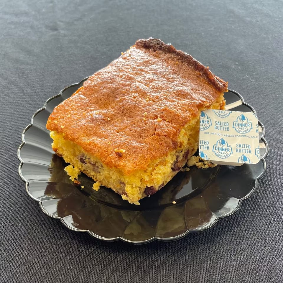 Aunt Berta's Kitchen's cornbread with a side of salted butter on a black scalloped plate.